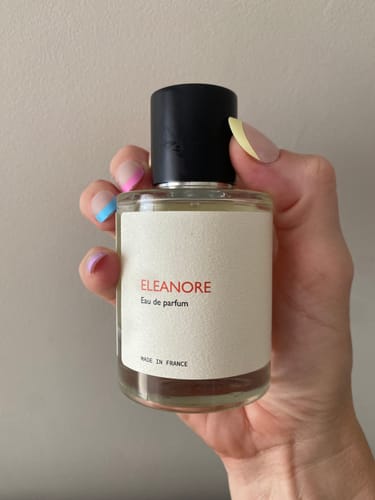 Customer holds up a bottle of Eleanore eau de parfum, showing its white label and black cap.