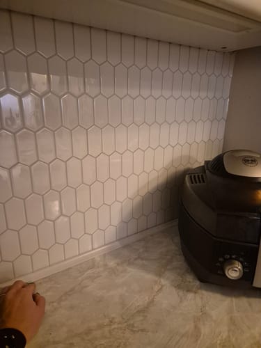 Kunde viser frem de nyinstallerte hvite Alexandra-veggflisene på en kjøkkenvegg over benkeplaten.