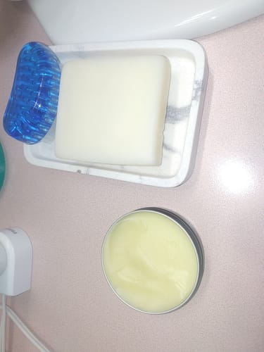 Reviewer's open tin of yellowish F-Balm on a counter next to a white bar of soap.