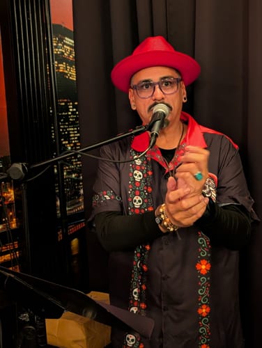 Reviewer wearing the El Sancho Clause Guayabera shirt and red hat while singing into a microphone.
