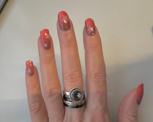 Hand einer Kundin mit den „Winter Rouge“ UV-Gel-Nagelfolien, die einen roten Ombré-Effekt und weiße Schneeflocken zeigen.