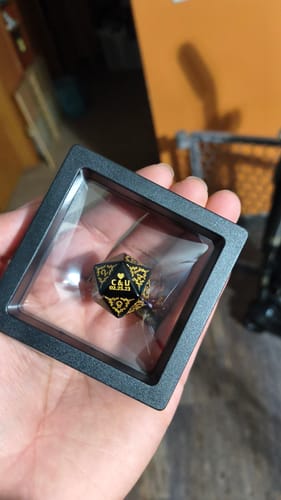 Reviewer holding the black and gold Dice Necklace inside its square display case.