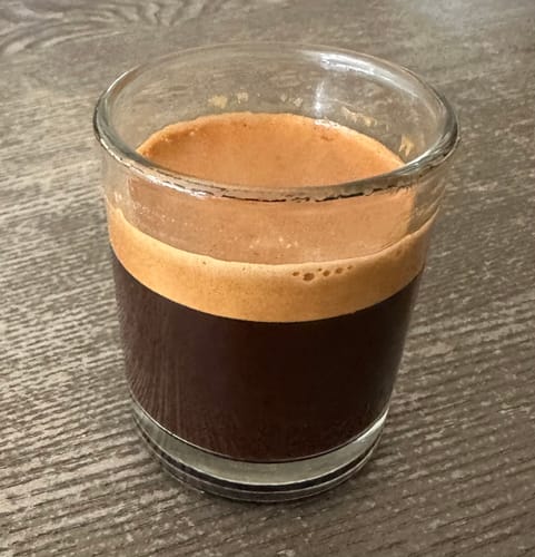 A reviewer's shot of Colombian Excelso espresso, showing a thick, rich crema in a glass cup.