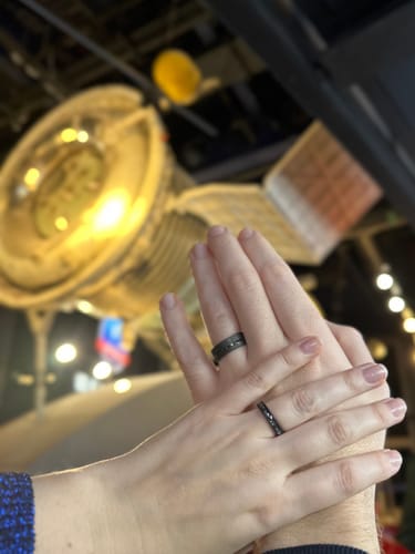 Reviewer's hands wearing the matching Black Meteorite Set rings in front of a space exhibit.