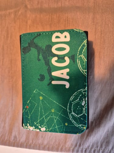 Kunde zeigt die geschlossene grüne Kindergeldbörse mit Fußball-Design, personalisiert mit dem Namen 'Jacob'.
