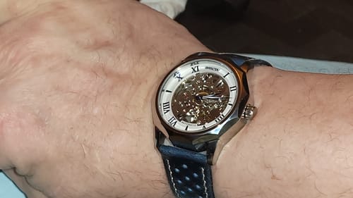 Reviewer's wrist showing the blue perforated Leather Sport Grip strap on a silver-toned skeleton watch.