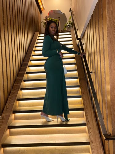 Reviewer posing on a lit staircase in the green Naked Mock Neck Drape Tie Dress.