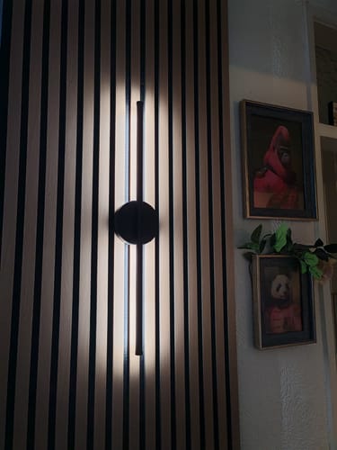 Customer's installed Acoustic Slatted Wall Panels with a modern light fixture creating a warm glow on the wood.