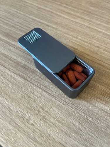 Reviewer's gray Nano Case with its lid slid open, showing pills inside on a wooden table.