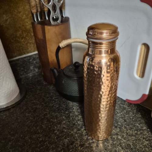 Reviewer's hand-hammered Pure Copper Water Bottle standing on a dark kitchen countertop.