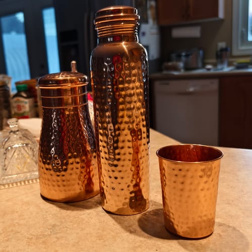 Customer's hand-hammered Pure Copper Water Bottle shown with a matching cup and vessel on a counter.