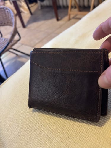 Customer holding their closed, dark brown Champlain Bison Bifold wallet on a light-colored surface.