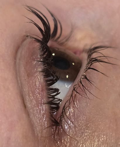 Close-up of a reviewer's eye with long, dark lashes that have been dramatically curled upwards from a lash lift.
