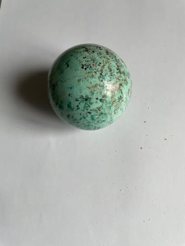 Photo d'un client de la sphère de Chrysocolle bleu-vert avec des taches sombres sur une surface blanche.