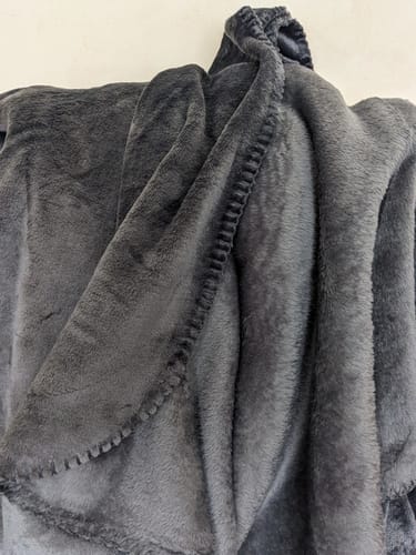 Close-up of the reviewer's dark grey Cuddle Fleece Blanket, showing the soft texture and stitched edge.