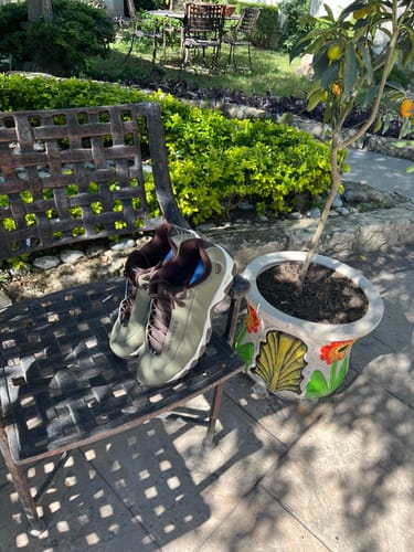 Customer's Burnt Olive ST329 CMF sneakers resting on a metal chair in a garden setting.