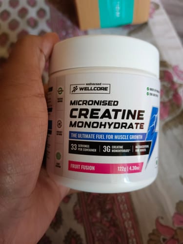 Customer holds a white tub of Wellcore Pure Micronised Creatine Monohydrate in Fruit Fusion flavor.
