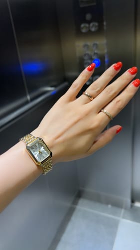 Customer showing their gold-colored CLAIRE DE MAINS watch on their wrist in an elevator.