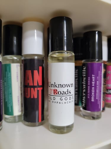 Reviewer's glass roll-on bottle of Unknown Roads perfume shown on a shelf with other scents.