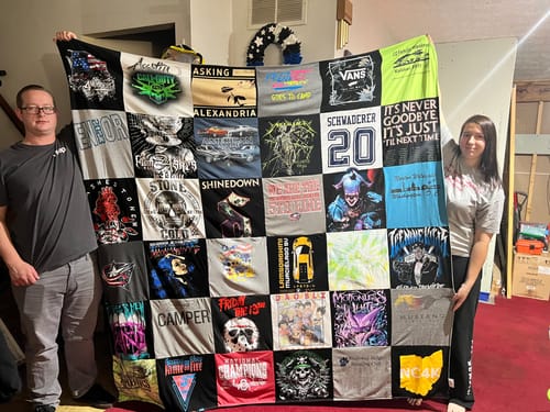 Two reviewers holding up their large, colorful Premium T Shirt Quilt made from many different shirts.