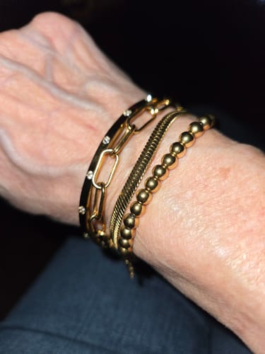 Close-up of a customer's wrist wearing several stacked gold-toned bracelets, including paperclip and beaded styles.