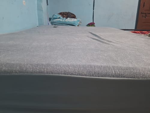 Customer's grey Flo mattress protector shown fitted snugly over a mattress in a bedroom.