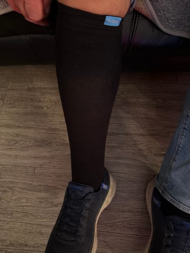 Customer's leg wearing a black Performance Eucalyptus Compression Sock with a blue sneaker.