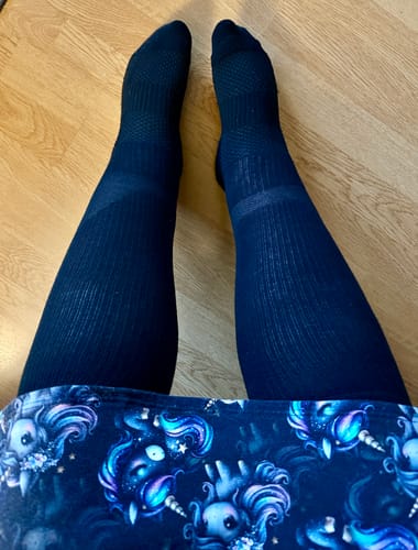 Kundens ben med svarta Diasocks breda stödstrumpor på, sedda uppifrån mot ett trägolv.