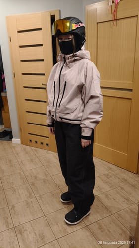 Reviewer standing indoors wearing the pink snow jacket with full ski gear, including a helmet and pants.