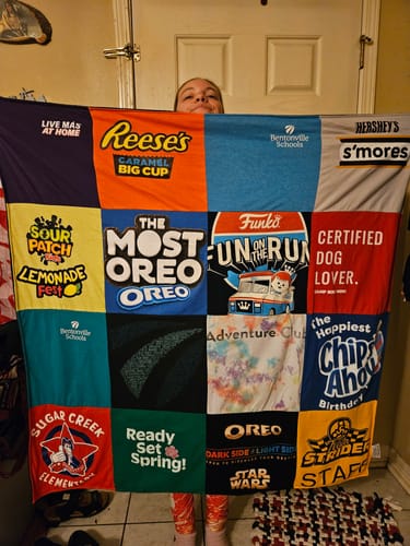 Customer holding up their colorful Premium T Shirt Quilt made from various t-shirts like Oreo and Reese's.