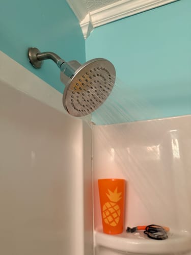 Customer's Gillian 6" Filtered Shower Head installed in a shower, spraying water with strong pressure against a blue wall.