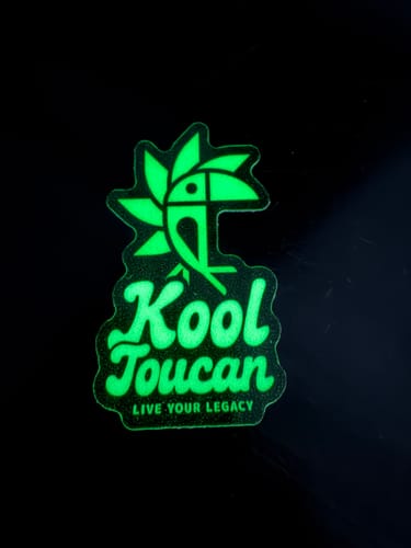 Customer's bright green glow-in-the-dark sticker with a "Kool Toucan" logo glowing against a black background.