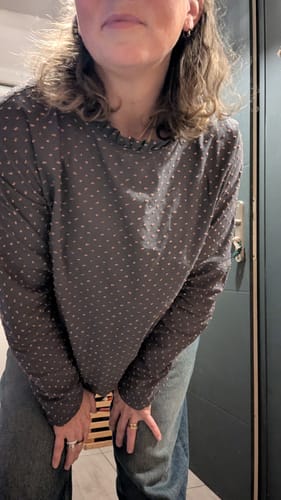 Cliente portant la Blouse Janelle grise à plumetis rose, montrant la coupe fluide.