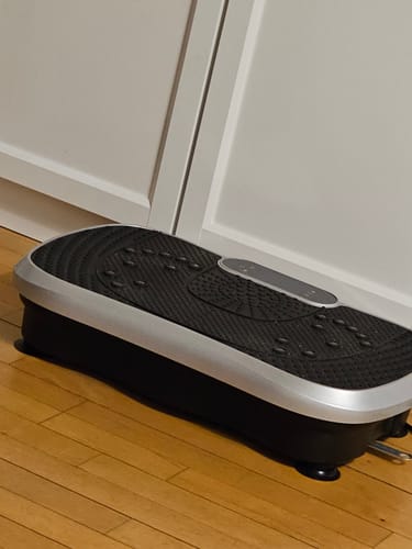 Kundes vibrationstræner med en tekstureret sort overflade, der står på et trægulv.