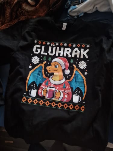 Kunde zeigt den schwarzen GLÜHRAK-Weihnachtspullover mit Drachen-Motiv, der flach liegt.