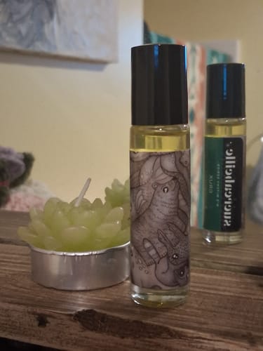 Customer's Crux perfume rollerball with an illustrated label on a wooden surface next to a candle.