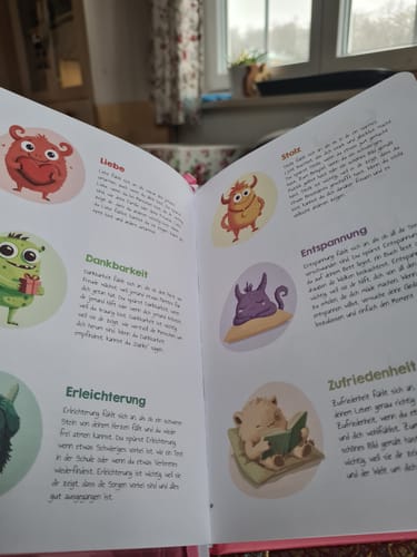 Ein Rezensent zeigt das aufgeschlagene Edubini Gefühlstagebuch mit bunten Illustrationen von verschiedenen Gefühlsmonstern.
