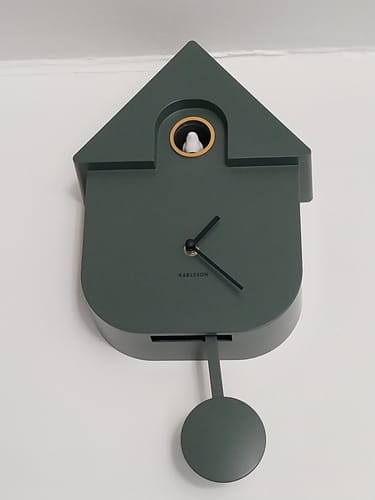 Klant toont de moderne, donkergroene Karlsson Cuckoo wandklok die aan de muur hangt.