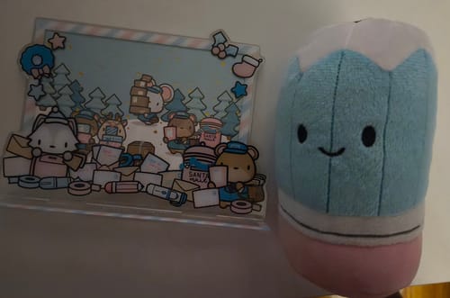 Close-up of a reviewer's acrylic standee and a small pencil plushie from the Holiday Happy Mail Advent Calendar.