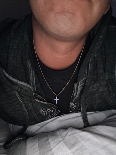 Close-up of a reviewer wearing the Mystery Gift, a light-colored cross pendant on a gold-tone chain.