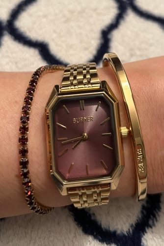 Reviewer's wrist showing the Violet Bracelet with purple stones, stacked next to a watch and a gold bangle.