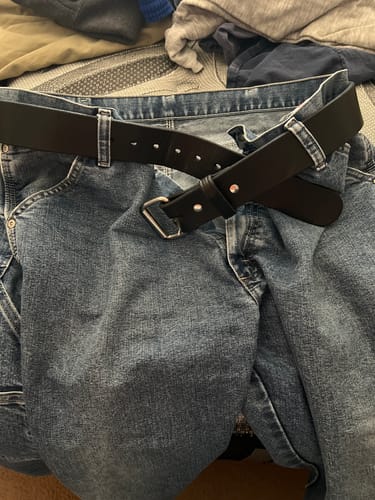 Customer's black Enforcer belt threaded through the loops of a pair of blue jeans lying on a bed.