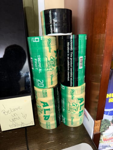 Reviewer's pyramid stack of several sleeves of ALP Tropical Fruit Nicotine Pouches on a desk.