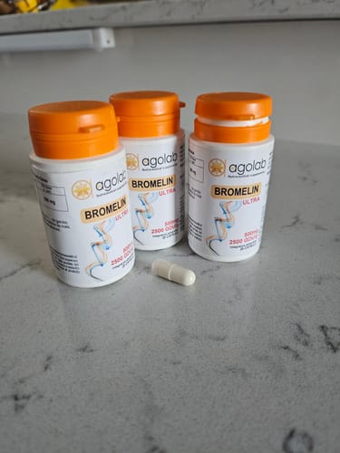 Recensore mostra tre flaconi di Bromelin Ultra e una capsula su un bancone.