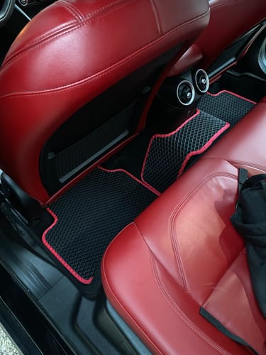 Recenzent pokazuje czarne, dopasowane dywaniki samochodowe z czerwoną lamówką w samochodzie z czerwoną skórzaną tapicerką.