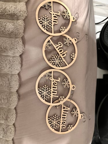 Customer's four personalized birch wood ornaments with names and snowflakes laid in a row on a soft surface.