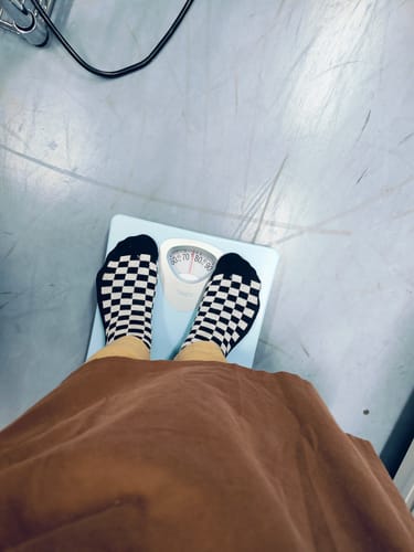 レビュー投稿者がアナログ体重計に立っている様子。針は約76kgを指しており、マンジャロ使用後の体重を示しています。