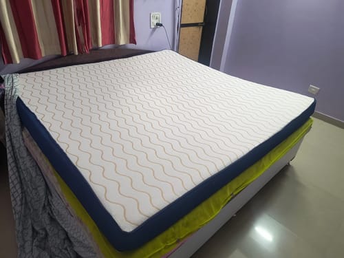 Customer's uncovered Flo Orthopedic Mattress on a bed, showing the white top with a wavy pattern and blue sides.