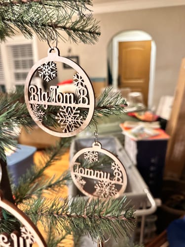 Close-up of a customer's personalized wooden ornaments with names and snowflakes hanging on a Christmas tree.