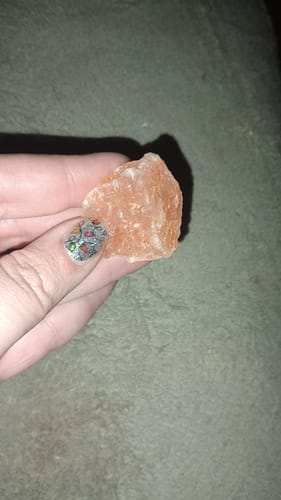 A customer's hand holding a rough, pink Natural Salt healing stone against a grey background.